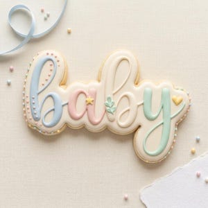 May include: A decorated sugar cookie in the shape of the word "baby". The letters are in pastel colors: blue, pink, and green, with a white background. The cookie is decorated with small dots and a star and leaf design.