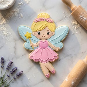 May include: A fairy-shaped biscuit decorated with pink icing for the dress, light blue wings, and a yellow star wand. The biscuit has a blonde bun and a floral crown. The background includes flour, lavender, and rolling pins.