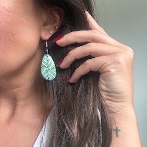 May include: A teardrop-shaped dangle earring featuring a mosaic pattern of light blue, turquoise, and silver-toned rectangular segments arranged in a woven, crisscross design. The earring hangs from a simple silver-toned metal hook wire.