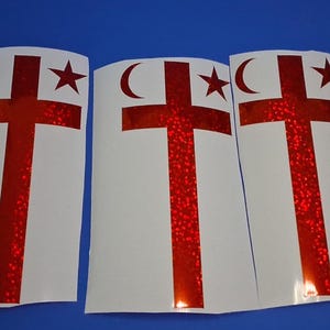 May include: Three identical rectangular white decals featuring a red holographic cross symbol. Each decal displays a crescent moon on the upper left side of the cross and a five-pointed star on the upper right side of the cross, all in red.