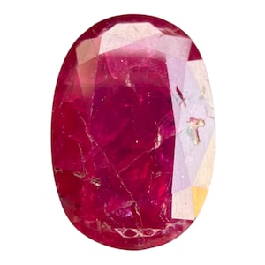 May include: Oval-shaped ruby gemstone with a faceted surface. The gem displays a deep red color with internal inclusions and a polished finish. The gemstone is set against a white background, highlighting its color and clarity.
