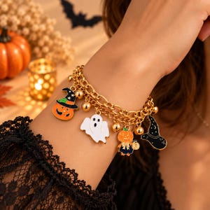 Könnte beinhalten: Ein goldfarbenes Gliederkettenarmband mit verschiedenen Halloween-Anhängern, darunter ein orangefarbener Kürbis mit Hexenhut, ein weißes Gespenst, eine Kürbisfigur in einem Kleid und ein schwarzer Hexenhut, ergänzt durch kleine goldene Perlen.