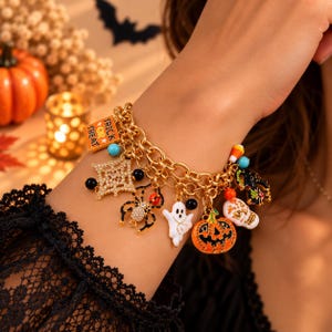 Op de afbeelding: Een goudkleurige bedelarmband met diverse Halloween-hangers, waaronder een vierkant oranje bordje met de tekst Trick or Treat, een spin, een spookje, een pompoen, een schedel, een zwarte kat en een fonkelende ster als bedel.