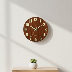May include: A round wooden wall clock with a dark brown finish. The clock features large, light-colored numerals and hands, with the word "QUARTZ" printed at the bottom. The clock is mounted on a white wall.