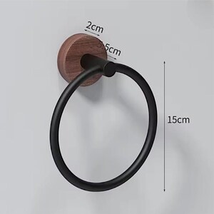 May include: A black towel ring with a wooden base, 5 cm in diameter, and a 15 cm ring. The wooden base is round and dark brown. The ring is made of black metal and is mounted on a light gray wall.