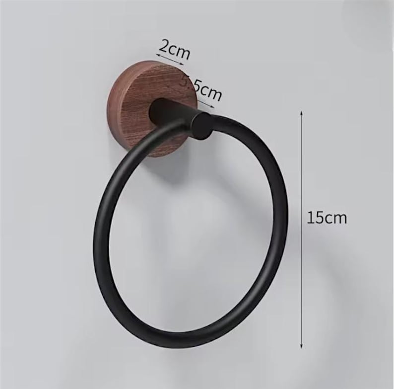 May include: A black towel ring with a wooden base, 5 cm in diameter, and a 15 cm ring. The wooden base is round and dark brown. The ring is made of black metal and is mounted on a light gray wall.