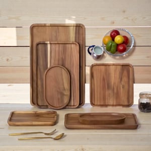 Puede incluir: Una colección de bandejas de madera para servir de varias formas y tamaños. Las bandejas son de madera de color marrón claro con vetas visibles. También hay un frutero de cristal, una jarrita y utensilios para servir.