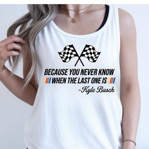 May include: White tank top with a black racerback design. The shirt features two crossed checkered flags and the quote, "BECAUSE YOU NEVER KNOW WHEN THE LAST ONE IS" by Kyle Busch, in black and colored text.
