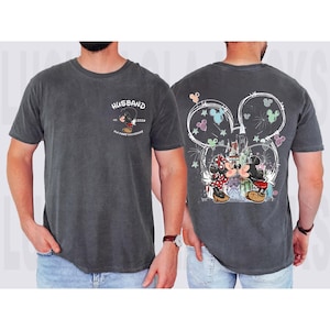 May include: Dark grey t-shirt with a Mickey Mouse and Minnie Mouse design. The front says "Husband" with a Mickey Mouse graphic and "Our First Anniversary". The back shows Mickey and Minnie kissing in front of a castle, with a Mickey Mouse ears outline.