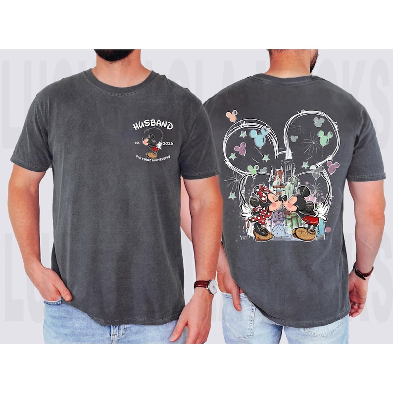 May include: Dark grey t-shirt with a Mickey Mouse and Minnie Mouse design. The front says "Husband" with a Mickey Mouse graphic and "Our First Anniversary". The back shows Mickey and Minnie kissing in front of a castle, with a Mickey Mouse ears outline.
