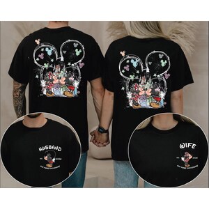May include: Black t-shirts with a Mickey and Minnie Mouse design, a castle, and fireworks. The back of the shirts have a large Mickey Mouse head outline with the couple in the centre. One shirt says "Husband" and the other says "Wife".