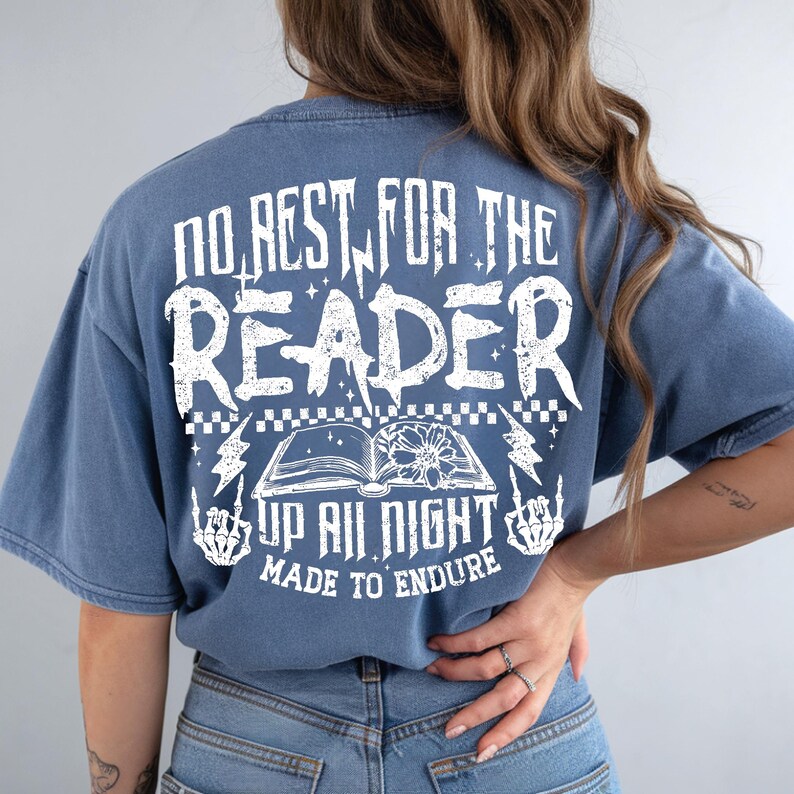 May include: Blue t-shirt with white graphic text: "NO REST FOR THE READER" above an open book illustration. Below the book are the words "UP ALL NIGHT MADE TO ENDURE". Lightning bolts and skeleton hands flank the book.