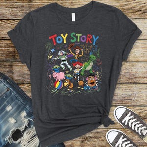 May include: Dark gray t-shirt featuring the words "Toy Story" in colorful letters above a graphic of the animated movie's characters. The design includes Woody, Buzz Lightyear, Rex, and other characters from the film.