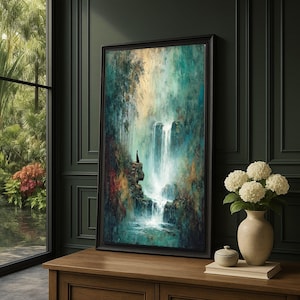 May include: A framed vertical wall art print depicting a waterfall cascading down rocky cliffs surrounded by lush foliage in shades of teal, green, and brown. A small silhouette figure stands on a ledge near the water, set in a black frame.