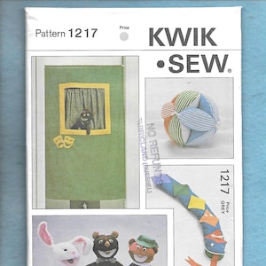 May include: A sewing pattern for a puppet show, featuring a puppet stage, three puppets, a ball, and a snake. The pattern is called "Kwik Sew" and the number is 1217. The pattern is for a grey color.