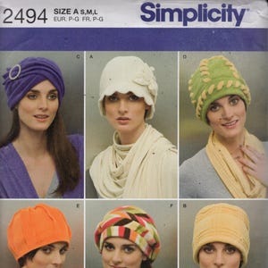 May include: Simplicity pattern 2494 featuring six different hat designs. The hats include a purple turban, a white cloche with a flower, a green hat with yellow trim, an orange hat, a colorful beret, and a yellow hat.