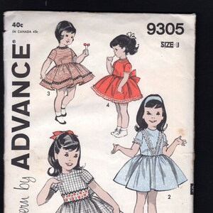 Könnte beinhalten: Ein Vintage-Schnittmuster für ein Mädchenkleid. Das Schnittmuster ist für Größe 11 und beinhaltet drei verschiedene Stile: ein rotes Kleid mit weißem Besatz, ein blaues Kleid mit weißen Punkten und ein kariertes Kleid mit rotem Besatz. Das Schnittmuster ist von Advance, einem Unternehmen für gedruckte Schnittmuster.
