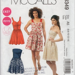 May include: McCall's sewing pattern M6349 featuring three dress designs. The pattern includes a red sundress, a floral print dress, and a blue and white patterned dress. The pattern is labeled as "Easy" and "Petite."