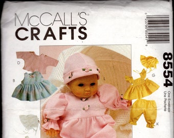 May include: A McCall's Crafts pattern envelope featuring a doll wearing a pink outfit with a matching hat. The envelope displays various doll clothing options, including dresses, pants, and tops. The number 8554 is visible on the envelope.