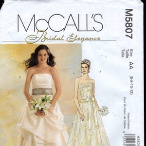 May include: McCall's Bridal Elegance sewing pattern M5807. The pattern features two strapless wedding dress designs. One dress has a draped skirt and embellished waist. The other is a lace gown with a ribbon belt.