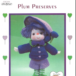 Könnte beinhalten: Häkelanleitung für eine lila Puppe mit einem blauen Hut und grünen Akzenten. Das Muster heißt "Plum Preserves" und stammt von "Lollipop Lane".