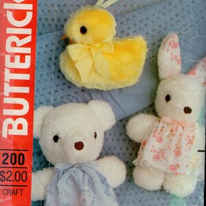 May include: A Butterick 200 craft pattern envelope featuring illustrations of three plush toys: a fuzzy yellow chick with a ribbon, a white teddy bear wearing a blue floral dress with lace trim, and a white rabbit in a pink floral dress with lace.