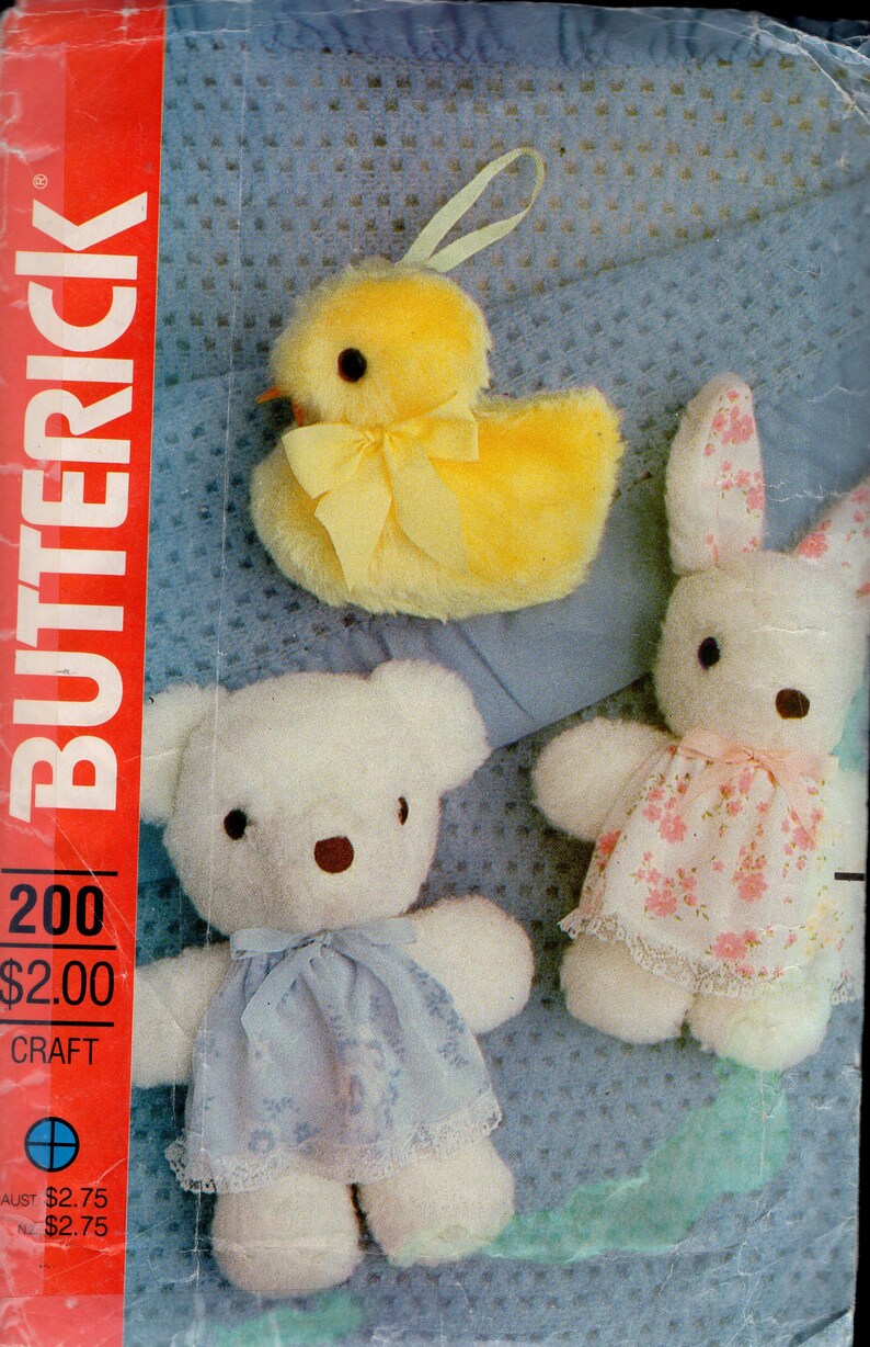 May include: A Butterick 200 craft pattern envelope featuring illustrations of three plush toys: a fuzzy yellow chick with a ribbon, a white teddy bear wearing a blue floral dress with lace trim, and a white rabbit in a pink floral dress with lace.
