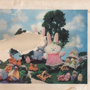 May include: A vintage Vogue Patterns sewing pattern for a bunny and duck. The pattern is for a one-size stuffed animal and features a pink bunny with a pink dress and a blue and white checked bunny. The pattern also includes a yellow duck with a pink beak and a yellow duck with a blue beak.