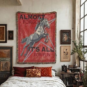 May include: A rectangular woven wall tapestry featuring a red background with a grey horse illustration, a large grey star outline, and the black text ALMOST FORGOT IT'S ALL FOR FUN. The tapestry has a fringed edge and is displayed on a wall.