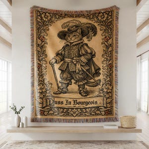 May include: A tapestry featuring a detailed illustration of a cat dressed in historical clothing, holding a cane and sword. The cat wears a feathered hat and is framed by a floral border. The text "Puss In Bourgeois" is displayed at the bottom.