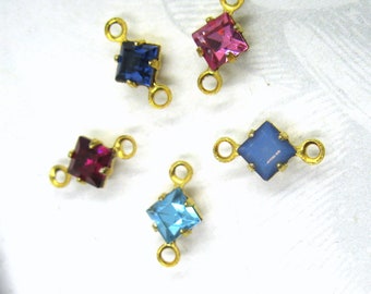 May include: Four gold-tone connector charms with square-shaped rhinestones. The rhinestones are in shades of blue, pink, red, and light blue.