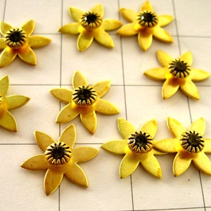 May include: Nine gold-coloured metal flower-shaped embellishments with black rhinestone centres.