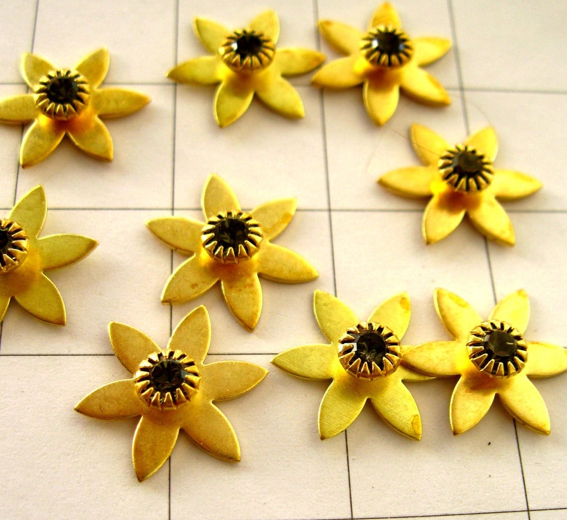 May include: Nine gold-coloured metal flower-shaped embellishments with black rhinestone centres.