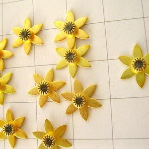 May include: Ten gold metal flower-shaped embellishments with black rhinestone centres.