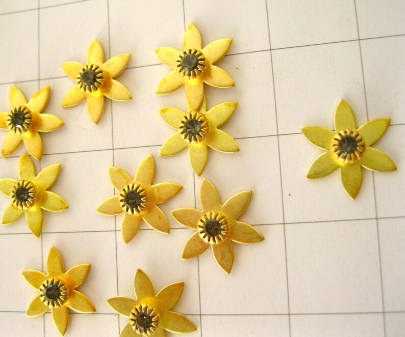 May include: Ten gold metal flower-shaped embellishments with black rhinestone centres.