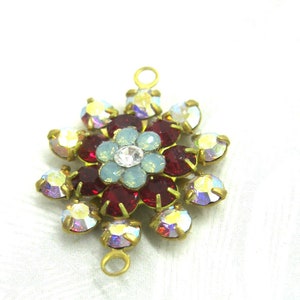 May include: A gold-toned metal flower charm with red, blue, and clear rhinestones. The charm has a loop on the top and bottom for attaching to jewelry.