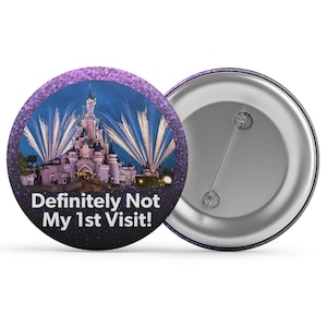 Könnte beinhalten: Ein runder Button mit einem lila Glitzerrahmen und einem Bild eines Schlosses mit Feuerwerk. Der Text "Definitely Not My 1st Visit!" ist auf dem Button aufgedruckt. Die Rückseite des Buttons ist silberfarben.