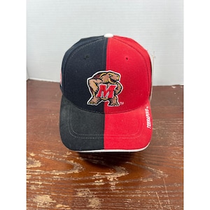 May include: A baseball cap featuring a split design with a black left side and a red right side. The front displays an embroidered turtle mascot logo with a red letter M on its chest. The word TERRAPINS is printed in white on the red side brim.