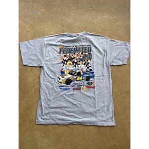 Puede incluir: Camiseta gris con un diseño de coche de carreras con el número 44, el texto "FEDERATED 250" y "NASHVILLE SPEEDWAY USA". El diseño incluye imágenes de pilotos de carreras y banderas a cuadros.