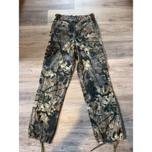 Puede incluir: Pantalones cargo de camuflaje en tonos verdes, marrones y beige. Los pantalones tienen m&uacute;ltiples bolsillos, cierre de bot&oacute;n y cremallera, y cordones ajustables en los tobillos. La tela tiene un patr&oacute;n de bosque realista.