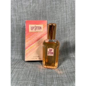 May include: A bottle of Lady Stetson cologne with a gold cap and a matching box. The box has the Lady Stetson logo and a peach and white background. The bottle is 1.0 fl oz (30ml).