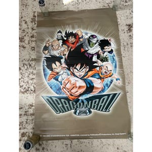 May include: A Dragon Ball Z poster featuring several characters in action poses. The poster has a tan background with a blue and white circular design behind the characters. The Dragon Ball Z logo is prominently displayed at the bottom.