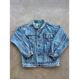 May include: Acid wash denim jacket with button closure, chest pockets, and buttoned cuffs. The jacket has a classic collar and a light blue and white color scheme. The jacket has a tag with a logo on the inside collar.