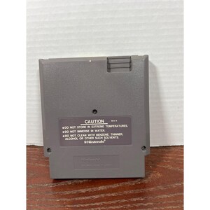 以下が含まれることがあります： グレーの任天堂ゲームカートリッジ。警告ラベルには「CAUTION」と書かれており、極端な温度や溶剤を避けるなど、お手入れ方法が記載されています。任天堂のロゴも表示されています。