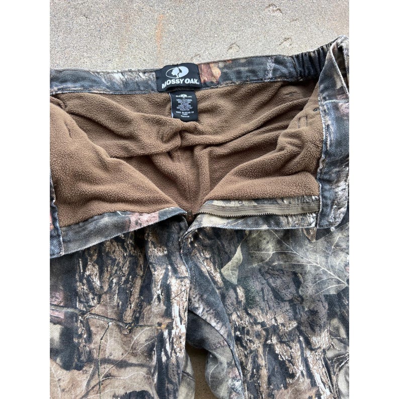 Pode incluir: Cal&ccedil;as de ca&ccedil;a camufladas com forro de l&atilde; castanha. As cal&ccedil;as apresentam fecho de correr e bot&atilde;o. O log&oacute;tipo Mossy Oak &eacute; vis&iacute;vel na cintura. Desenhadas para atividades ao ar livre.