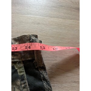 Puede incluir: Primer plano de una tela con estampado de camuflaje con una cinta m&eacute;trica rosa estirada sobre ella. La cinta lee de 33 a 40 cm. La tela parece ser parte de una prenda, posiblemente pantalones cortos o largos.