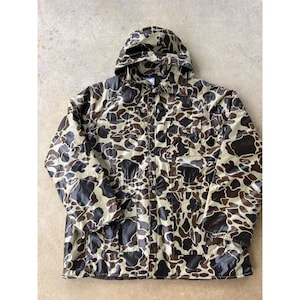 May include: A hooded jacket featuring a brown and tan camouflage pattern. The jacket includes a front button closure, long sleeves, and two rectangular chest pockets. The material has a smooth, slightly reflective finish throughout the garment.