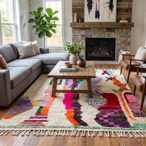 May include: A rectangular area rug featuring a cream-colored base with an abstract pattern of vibrant, multi-colored shapes in shades of hot pink, orange, purple, and teal, finished with a knotted fringe along the shorter edges.