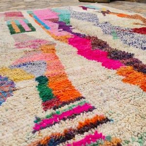 May include: A thick, off-white area rug featuring a high-pile texture and an abstract pattern of vibrant, multi-colored geometric shapes and lines in shades of hot pink, bright orange, deep purple, turquoise, yellow, and red across the surface.