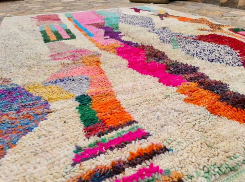 May include: A thick, off-white area rug featuring a high-pile texture and an abstract pattern of vibrant, multi-colored geometric shapes and lines in shades of hot pink, bright orange, deep purple, turquoise, yellow, and red across the surface.